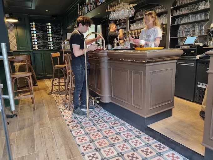 Les carreaux de ciment au pied du bar central, tabourets de bois et ardoise des bières.