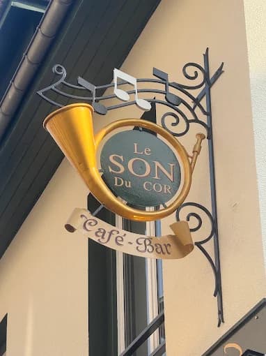 L'enseigne du Son du Cor : un cor de chasse doré sur une potence de fer forgé, avec le mot Café-Bar sur une banderole.